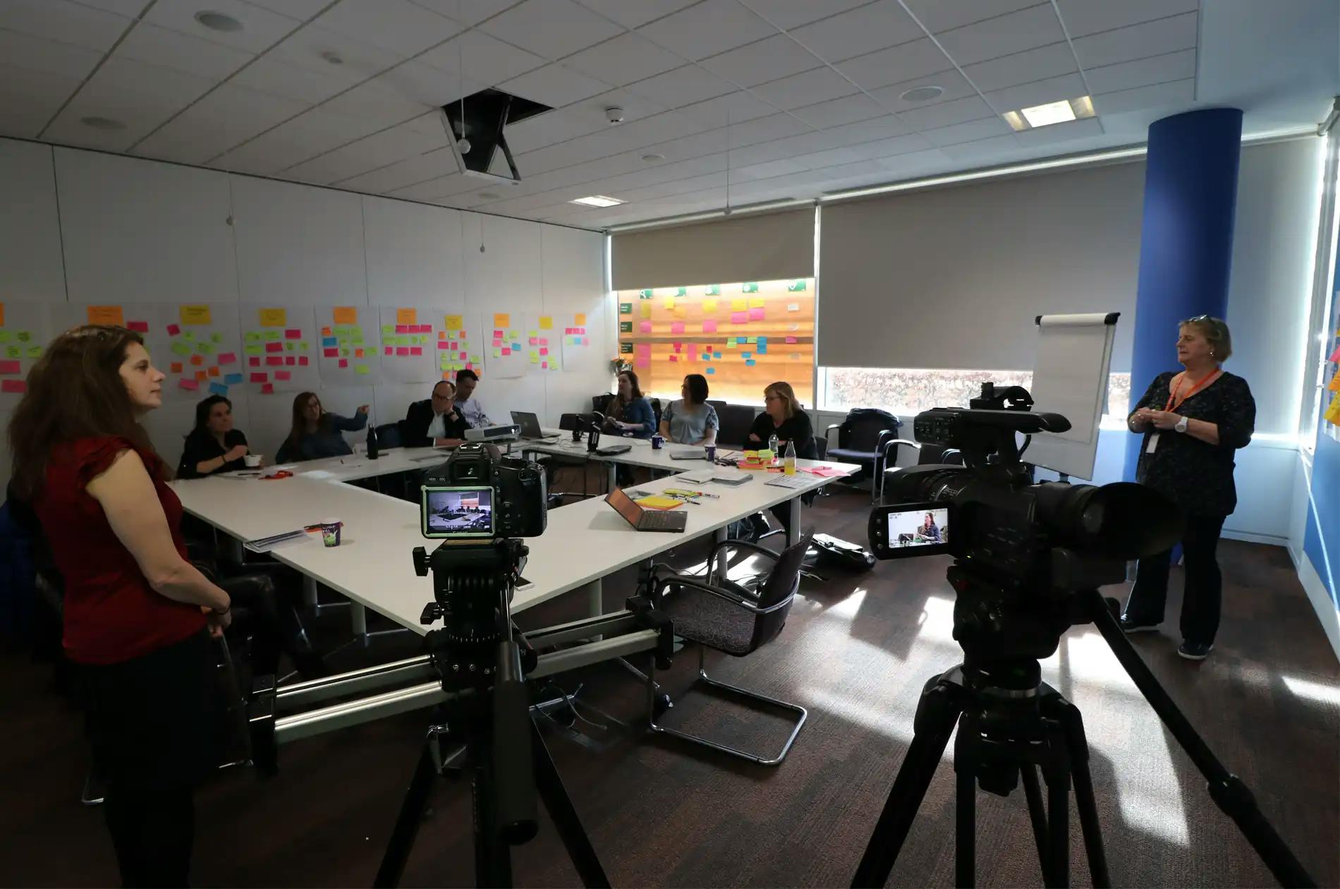 Wide shot of conference with cameras in foreground